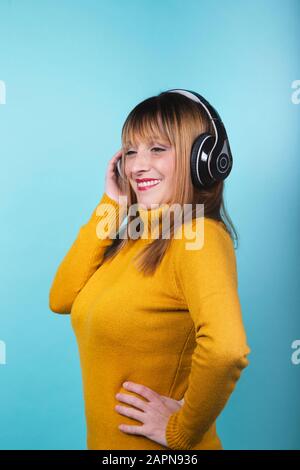 Femme en jaune pullover souriant avec casque écoutant de la musique souriant sur fond bleu. Image isolée. Banque D'Images