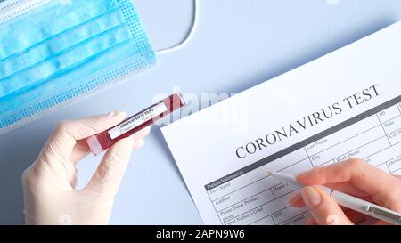 Concept de test sanguin du coronavirus. Mains d'infirmière tenant le tube à essai avec du sang du patient pour l'analyse 2019-nCoV et remplit le formulaire médical en laboratoire. C Banque D'Images
