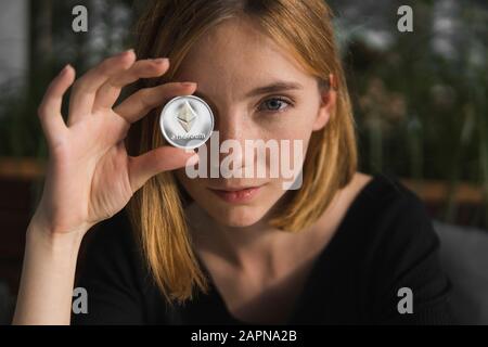 Une belle fille est en joignant une pièce d'or et d'argent à l'Ethereum son œil. Les Bitcoins, crypto monnaie, l'argent électronique. Woman sitting in cafe holding Banque D'Images