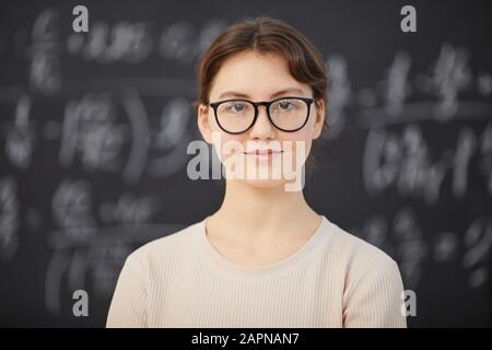 Portrait de professeur de maths féminin dans des lunettes regardant la caméra avec tableau noir en arrière-plan Banque D'Images