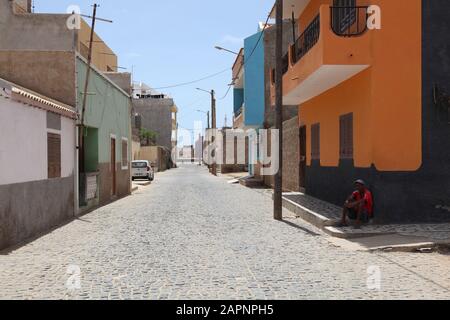 Une rue principale déserte à l'heure de la siesta avec un homme local reposant à l'ombre à côté de la route à Santa Maria, Sal, Cap Vert, Afrique Banque D'Images