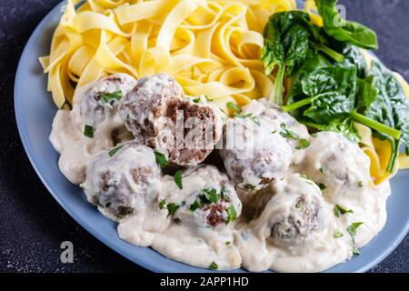 Boulettes de viande suédoise classiques servies avec des nouilles aux œufs et des feuilles d'épinards fraîches sur une plaque sur une table de cuisine en béton, vue horizontale d'en haut, gros plan Banque D'Images