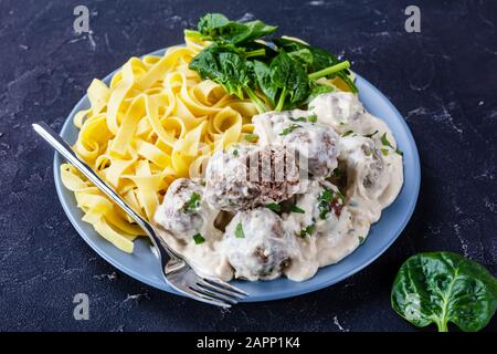 Boulettes de viande suédoise classiques servies avec des nouilles aux œufs et des feuilles d'épinards fraîches sur une plaque sur une table de cuisine en béton, vue de dessus, gros plan Banque D'Images