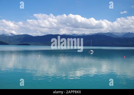 Un beau lac bleu avec des montagnes boisées à l'horizon, lors d'une journée d'été ensoleillée. Sur l'eau, il y a un seul bateau à voile. Banque D'Images
