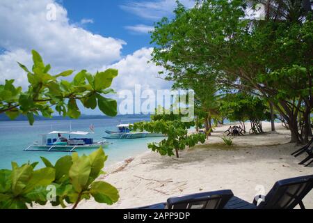 Une petite île dans l'archipel des Philippines. Il y a deux bateaux à la scie garés près de la plage de sable. L'océan est calme, il est ensoleillé et chaud. Banque D'Images