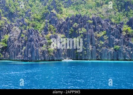 Un bateau à parachute solitaire naviguant près de la grande île rocheuse de l'archipel des Philippines. L'eau de l'océan est calme et légèrement ondulée. Banque D'Images