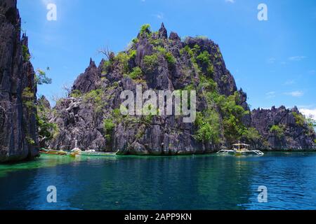 Paraw (double outrigger) bateaux naviguant près de la grande île rocheuse dans l'archipel des Philippines. L'eau de l'océan est calme et légèrement ondulée. Banque D'Images