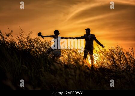 Juste marié amoureux couple hipster dans la robe de mariage et costume sur le terrain au coucher du soleil. Heureuse mariée et marié dans la prairie d'été. Romantique Marié jeune fa Banque D'Images