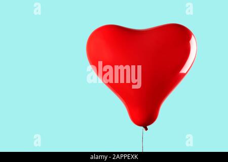 un ballon rouge gonflé en forme de coeur contre un fond bleu pâle ou bleu avec un espace vide sur la gauche Banque D'Images