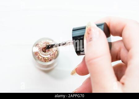 Mains féminines faisant manucure, vernis à ongles en couleur glitter or sur un fond blanc. Concept de salon de soins de la peau et des ongles Banque D'Images