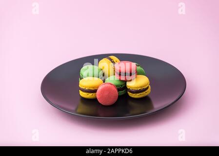 Délicieux macarons français dans une plaque noire sur fond rose pastel. Macarons rouges, jaunes et verts Banque D'Images