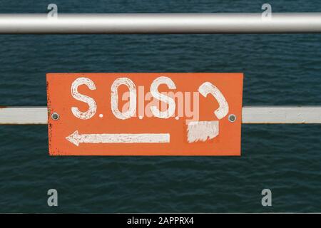 Signe rugueux et résisté pointant vers un téléphone SOS pour permettre au public de contacter le garde-côtes sur une plage Banque D'Images
