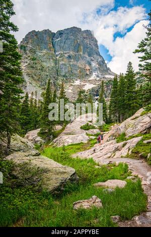 Une paire de randonneurs sur la piste boisée d'Emerald Lake, Rocky Mountain National Park, CO. Pics de montagne avec neige inégale et nuages au-dessus de la tour. Banque D'Images