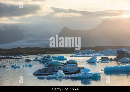 Les icebergs Jokulsarlon glacial lagoon lors d'un coucher de soleil rouge vibrant repose immobile comme il est entouré par l'eau de mer froide. Banque D'Images