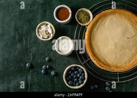 Cheesecake maison à base de sucre de canne sur portoir de refroidissement avec une variété de garnitures dans des bols en céramique sur fond sombre de texture. Plat, espace Banque D'Images