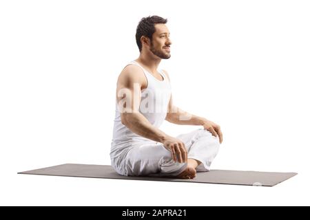 Guy vêtu de blanc assis sur un tapis d'exercice avec des jambes croisées isolées sur fond blanc Banque D'Images