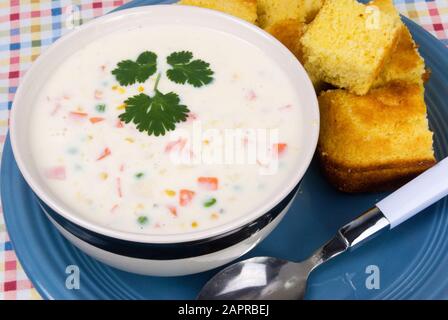 Un bol de soupe de chaudrée maison saupoudrée de persil italien plat sur le dessus et servi avec du pain de maïs jaune chaud frais. Banque D'Images