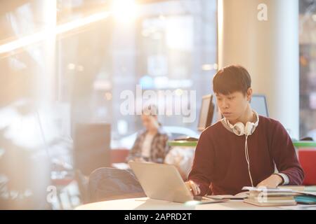 Étudiant universitaire asiatique utilisant un ordinateur portable tout en étant assis à la table de la bibliothèque Banque D'Images