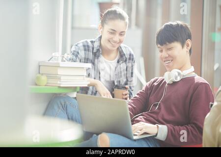 Un homme asiatique dans un casque assis à taper sur un ordinateur portable et à sourire, il se prépare à faire ses devoirs avec une jeune femme Banque D'Images