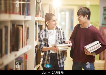 Deux amis tenant des livres souriant une conversation l'un avec l'autre tout en marchant le long des librairies dans la bibliothèque Banque D'Images