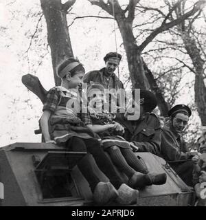 Pendant la libération des Pays-Bas à la fin de la seconde Guerre mondiale, quelques enfants sont assis sous l'approbation de quelques soldats/soldats sur un véhicule de char/armée. Pays-Bas, Amersfoort, 1945. Banque D'Images