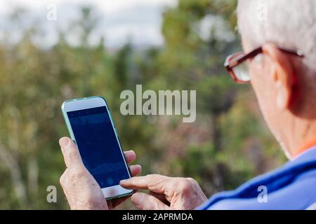 Vue arrière de l'homme âgé avec des lunettes prenant une photo avec le mobile Banque D'Images