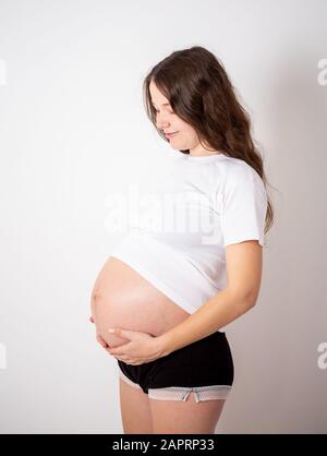 La jeune belle femme enceinte éprouve de fortes émotions sur un fond blanc Banque D'Images