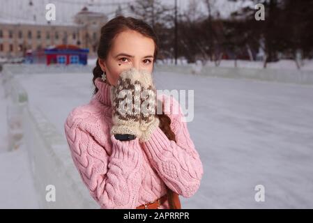 Jeune femme en hiver rose peignes se tient à la patinoire extérieure en plein air Banque D'Images