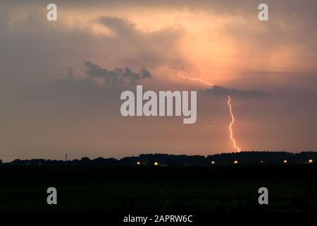 Un éclair de couleur rouge frappe d'un orage éloigné Banque D'Images