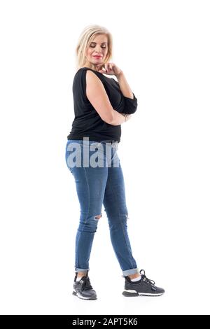 Vue latérale d'une femme d'âge moyen réfléchie dans des vêtements décontractés regardant vers le bas pensif. Longueur totale du corps isolée sur fond blanc. Banque D'Images