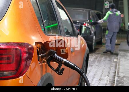 Remplir la voiture de diesel à la station-service. Pompage du carburant diesel dans une voiture orange à la station-service en soirée. Banque D'Images