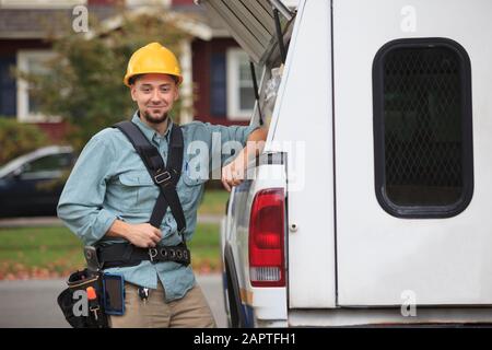 Un ouvrier professionnel récupère les fournitures à partir d'une trappe ouverte sur le côté de son camion de travail Banque D'Images