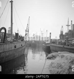 Port avec barges, remorqueurs, grues et un cargo en arrière-plan Date: Non daté mots clés: Barges, ports, navires de fret Banque D'Images