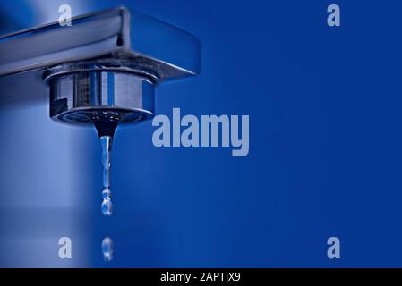 Une goutte d'eau s'écoule d'un robinet d'eau contre une tuile bleue. Espace de copie. Banque D'Images