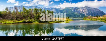 Panorama de paysage de montagne et d'île d'arbres reflétant un lac fixe avec ciel bleu et nuages, parc national des Lacs-Waterton Banque D'Images