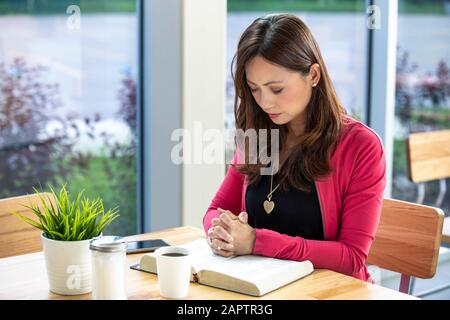 Une femme asiatique mûre priant, après avoir fait une étude biblique personnelle, dans un café; Edmonton, Alberta, Canada Banque D'Images