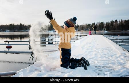 Garçon jetant de la neige dans les airs tout en jouant au bord de l'eau en Suède Banque D'Images