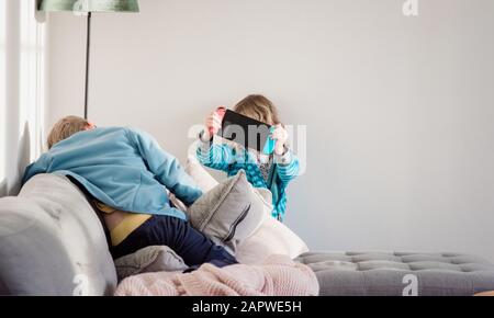 Frère et sœur jouant Nintendo Switch à la maison sur le canapé Banque D'Images