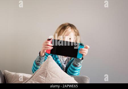 Une jeune fille jouant à Nintendo Switch à la maison sur le canapé Banque D'Images