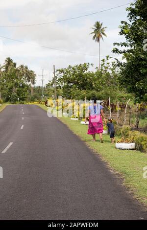 Samoan femme avec enfant, marchant à côté d'une route vide Banque D'Images