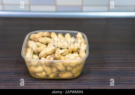 Boîte en plastique remplie d'arachides sur une surface en bois Banque D'Images
