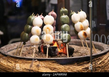 Le dango vert, violet et blanc (boulettes de riz mochi japonais) rôtie sur des brochettes au-dessus de coals chauds. Banque D'Images