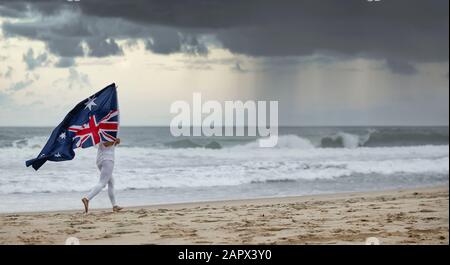 Drapeau australien soufflant dans le vent tenu par une femelle jogging sur une plage Aussie, Banque D'Images