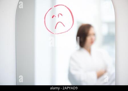 Visage bouleversé dessiné par rouge ou rouge rouge rouge rouge à lèvres sur le miroir sur le fond de la fille triste Banque D'Images