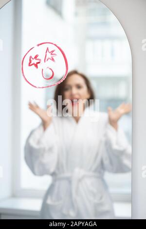 Jeune femme hurlant devant le miroir avec un visage choqué dessiné avec rouge à lèvres Banque D'Images