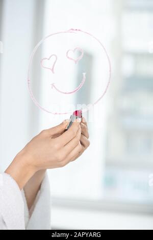 Main de fille avec rouge à lèvres cramoisi dessin visage avec sourire et yeux en forme de coeur Banque D'Images