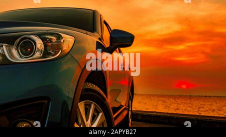 Voiture SUV compacte bleue avec sport et design moderne garée sur route en béton près de la plage de la mer au coucher du soleil. Vue avant de la voiture de luxe. Nouvelle voiture SUV Banque D'Images