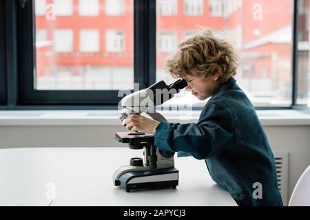 Un écolier intelligent ou un biologiste se pendu sur le bureau tout en regardant au microscope Banque D'Images