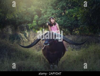 Femme asiatique qui monte du buffle avec la radio Banque D'Images