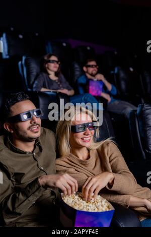 Bonne date dans les lunettes en relief mangeant du popcorn tout en étant assis devant l'écran Banque D'Images